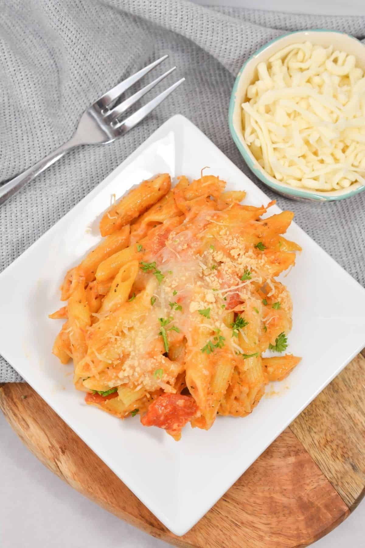 Baked pepperoni pizza mac and cheese served on a plate with a fork and grated cheese on the side.