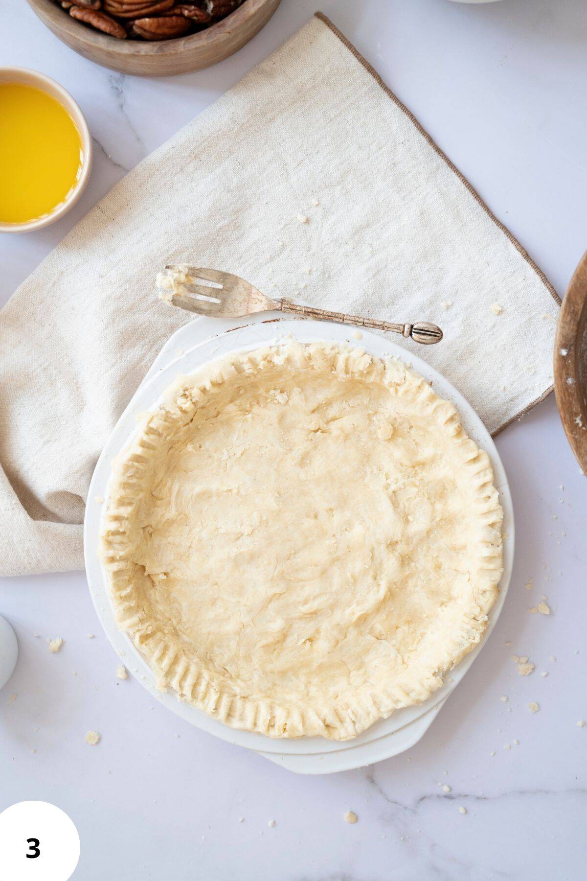 Pie crust shaped in a pan with baking ingredients placed on the side.