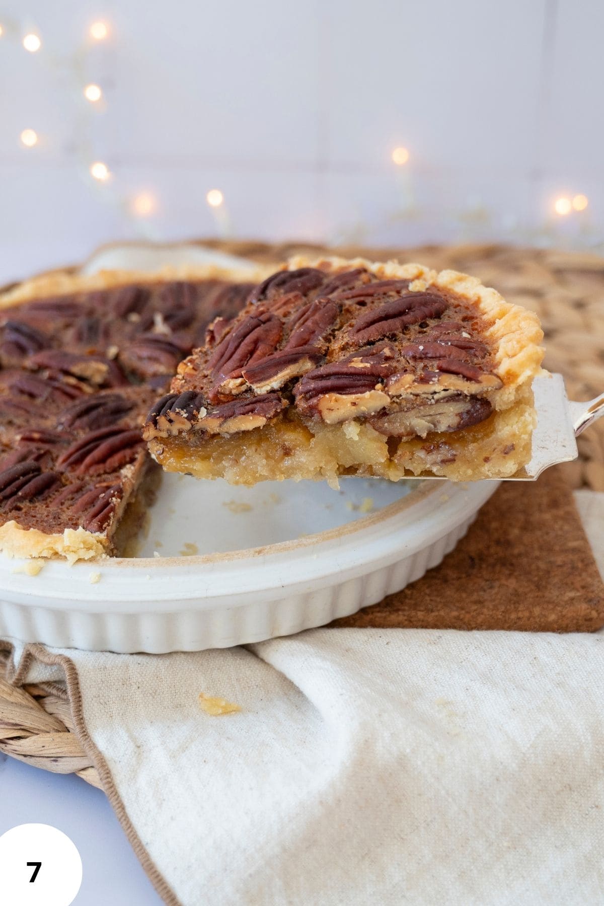 A hand taking a slice of pecan pie from the serving dish.