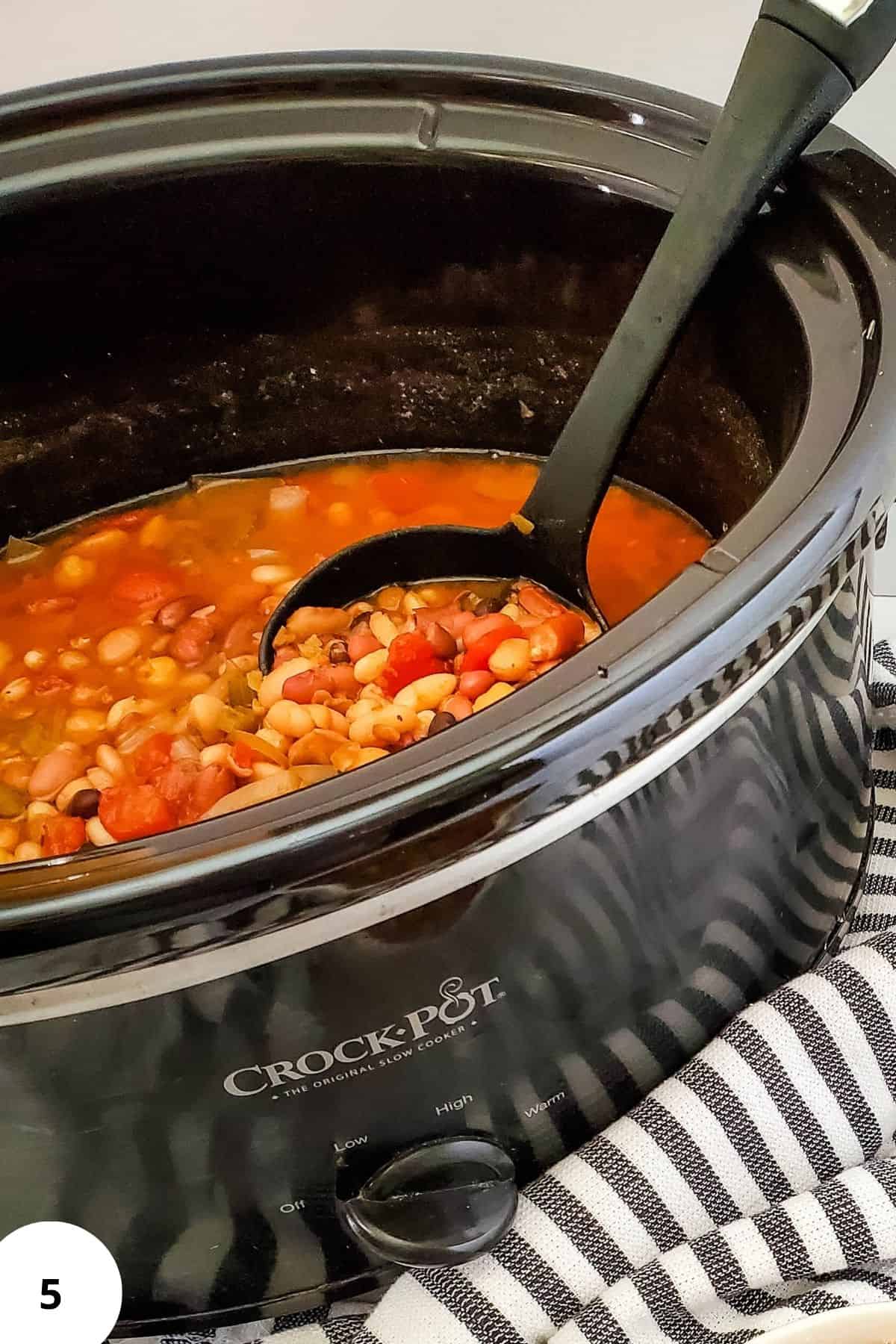 A crockpot filled with vegan bean soup with a ladle resting inside.