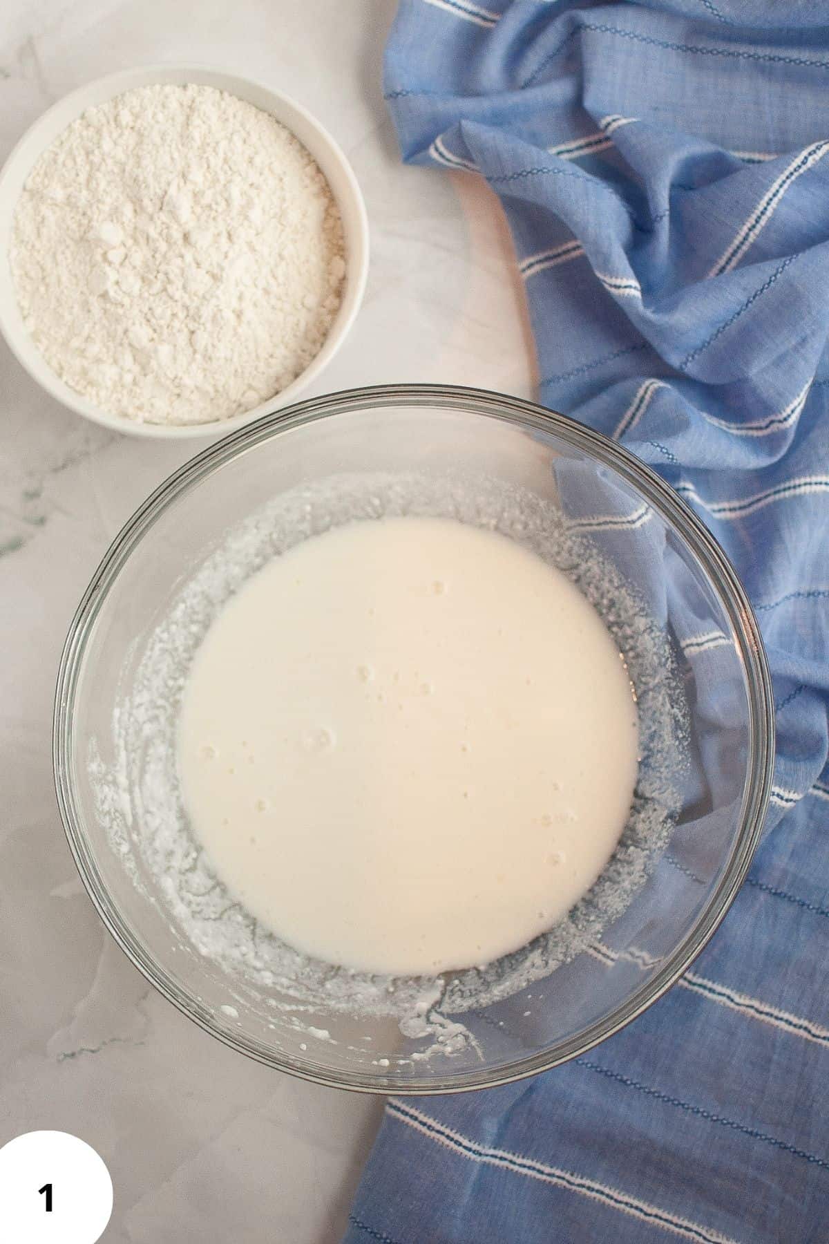 Two bowls, one with sourdough starter and one with flour, placed on a table with a tablecloth beside them.