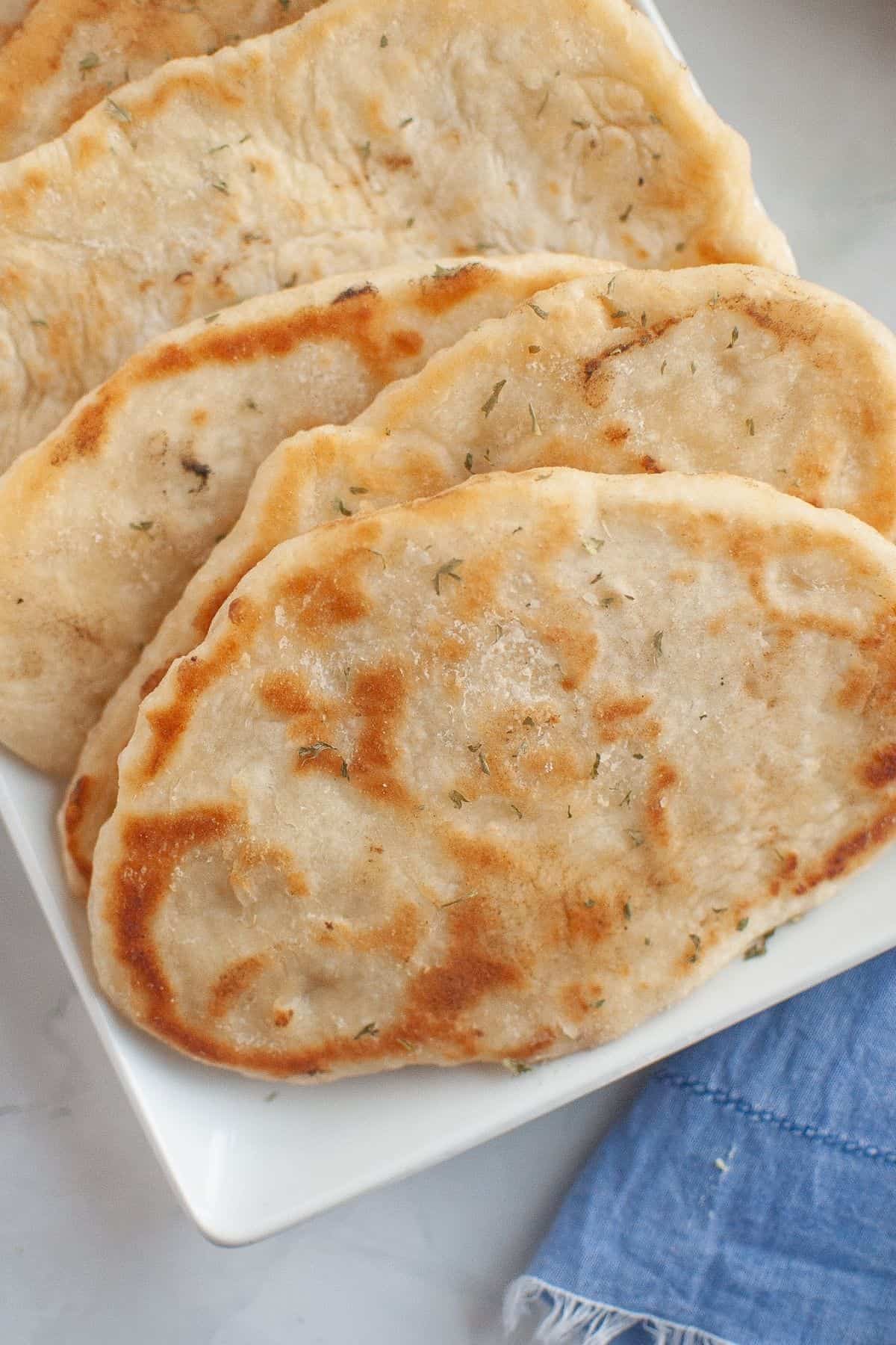 Close-up look of a golden-brown homemade flatbreads on a white rectangular plate with rolling pin and salt shaker.