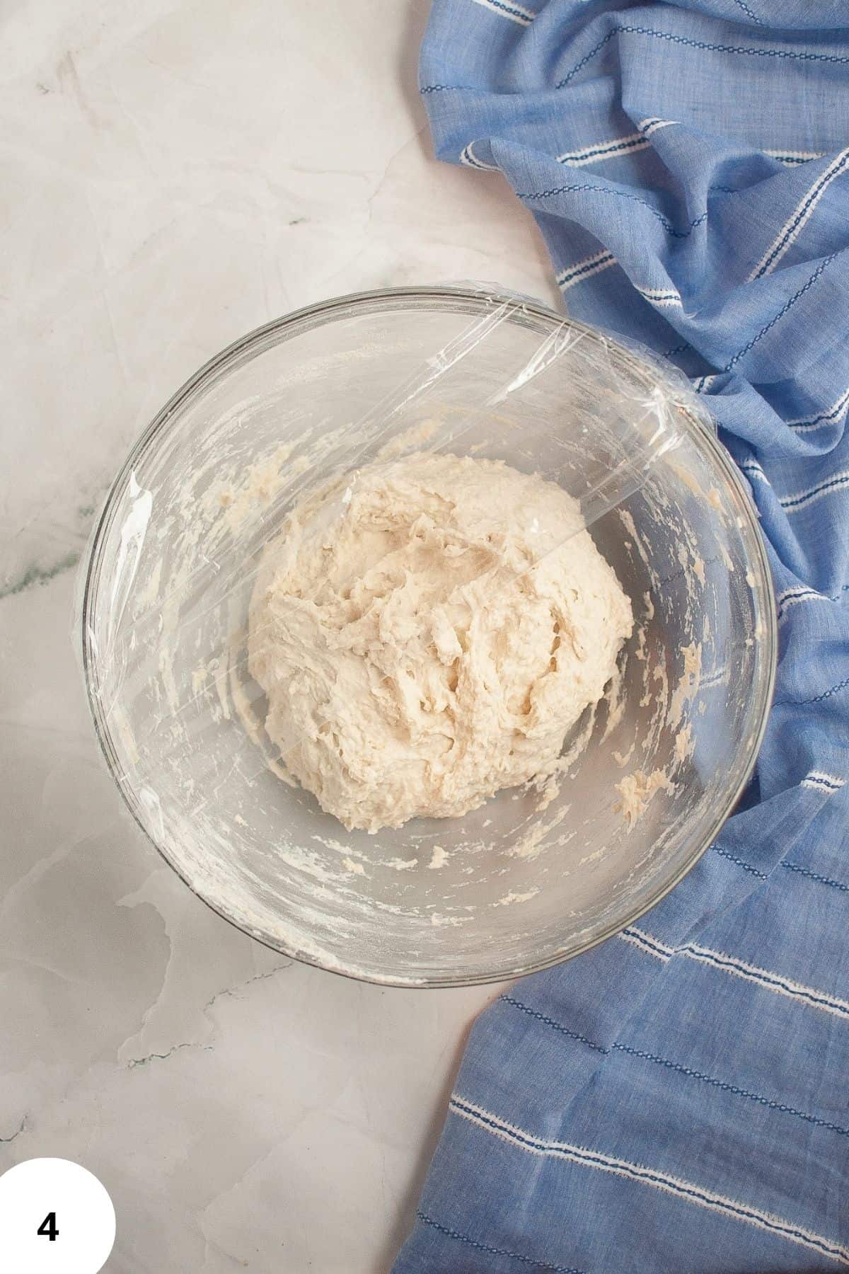 Active sourdough starter in a large bowl, partially covered with plastic on the edge.