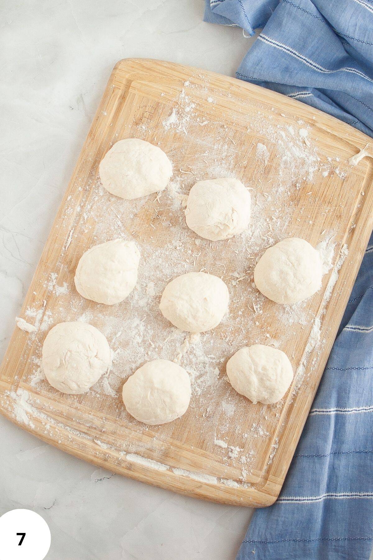 Dough being placed on a floured wooden board with a tablecloth on the side.