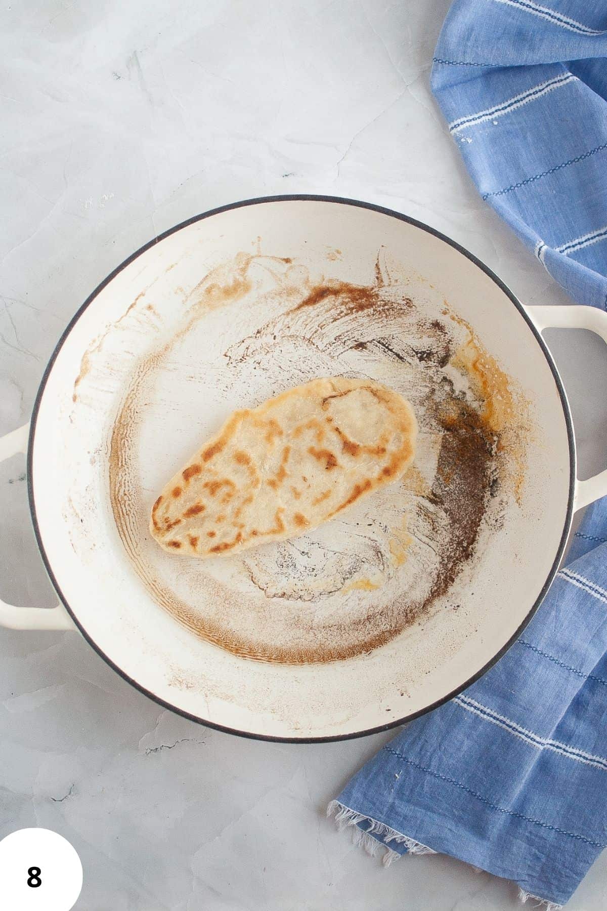 A skillet with naan cooking in it, with a tablecloth visible on the side.