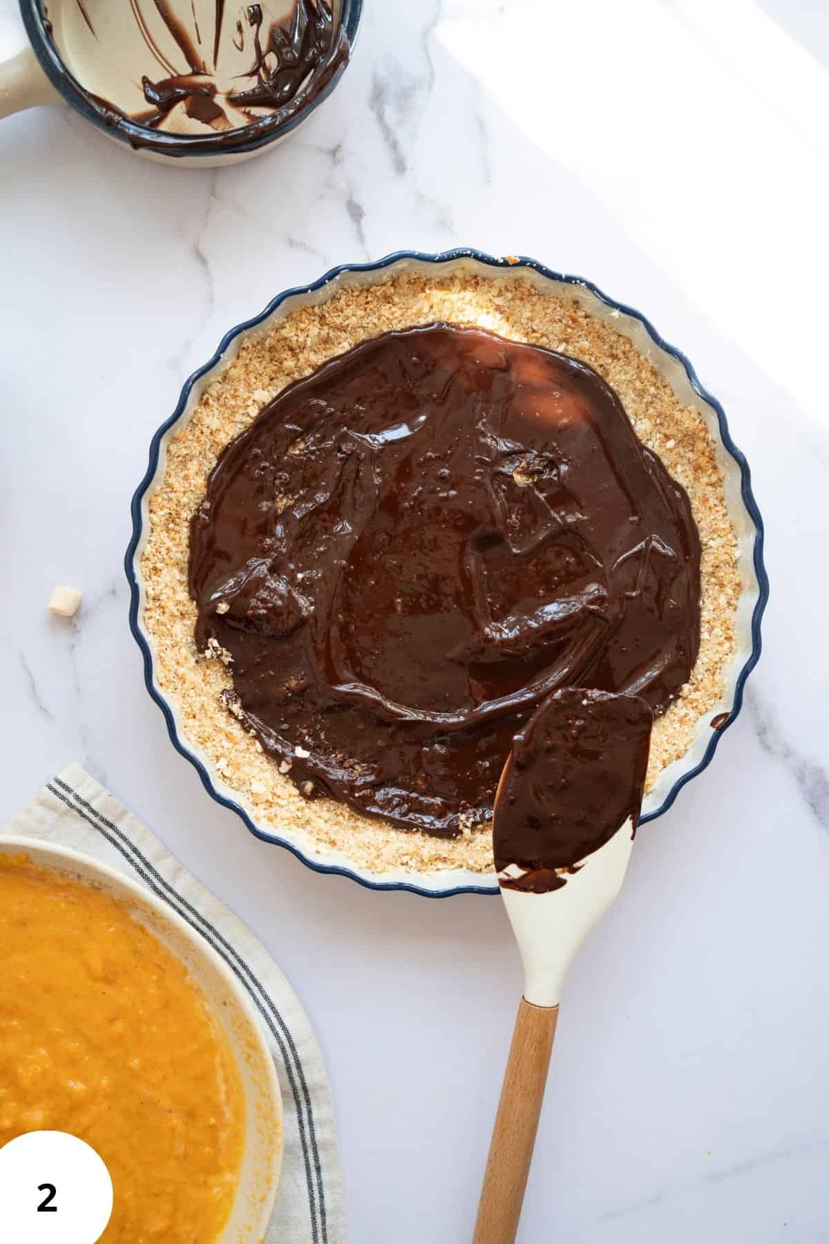 Dark melted chocolate being spread over the pie crust with a spatula.