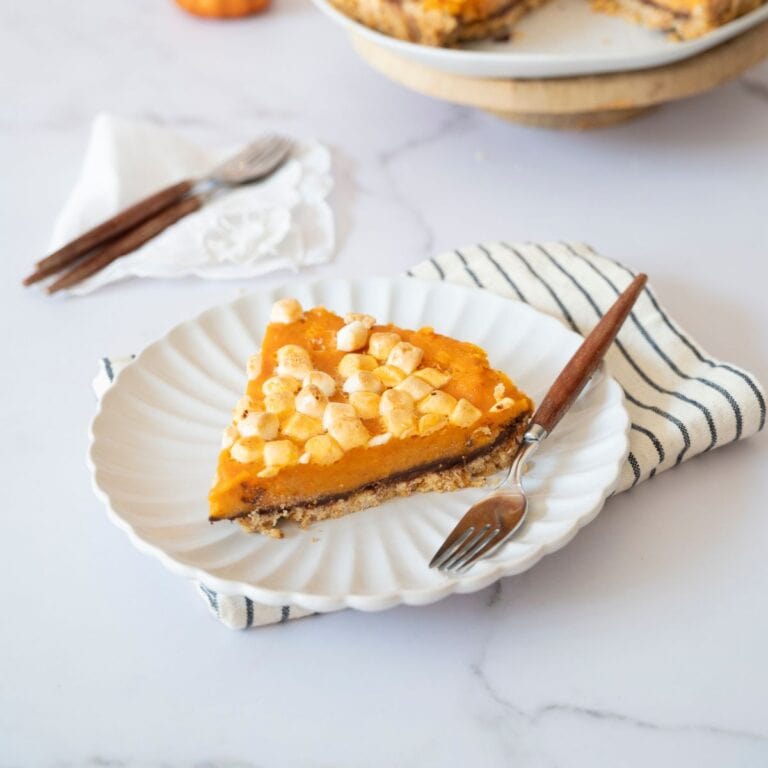 Slice of sweet potato pie on a plate with a table napkin underneath and a fork on the side.