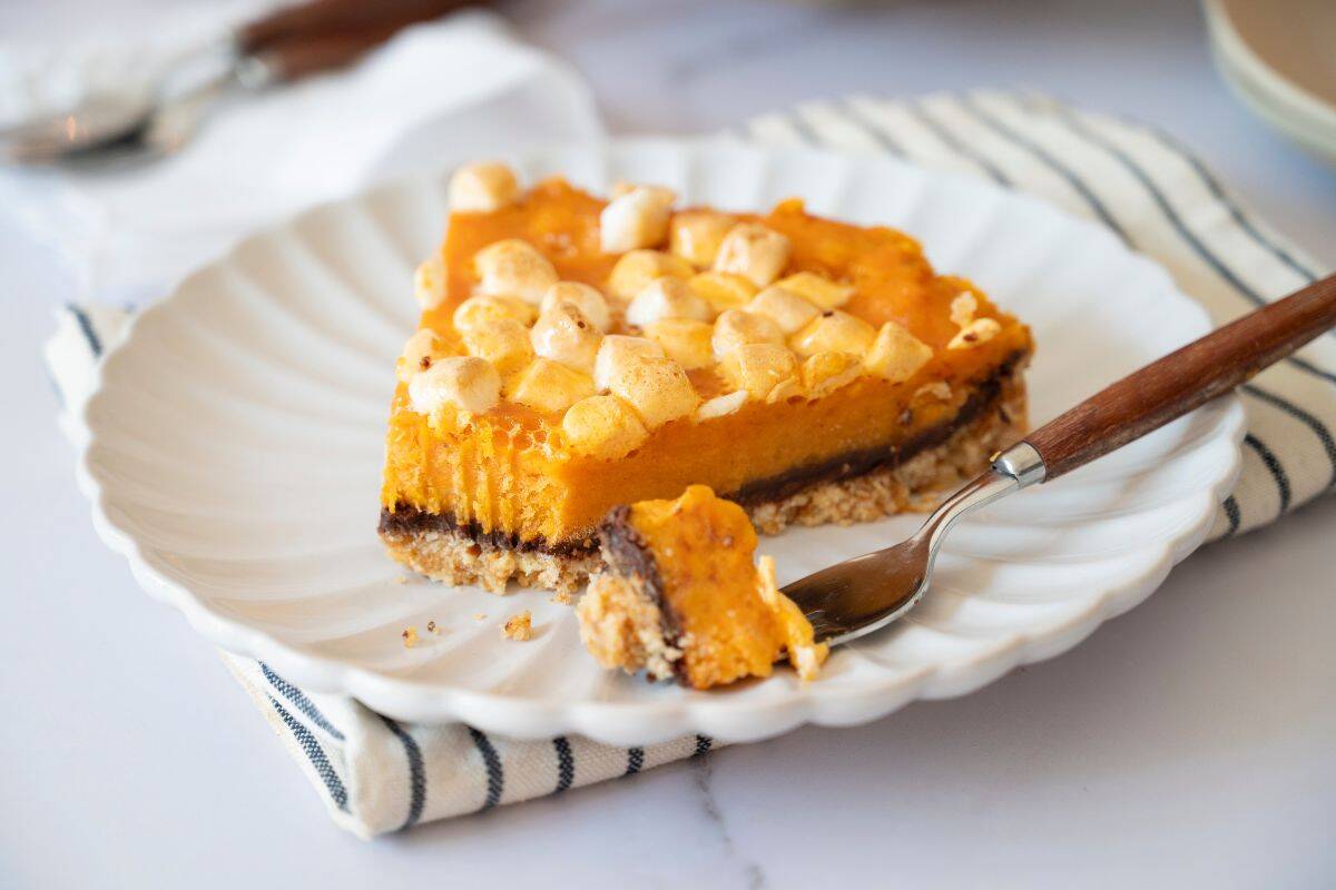 Slice of sweet potato pie on a plate with a table napkin underneath and a fork on the side.
