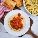 Spaghetti served on a plate with a side of bread and a bowl of pasta in the background.