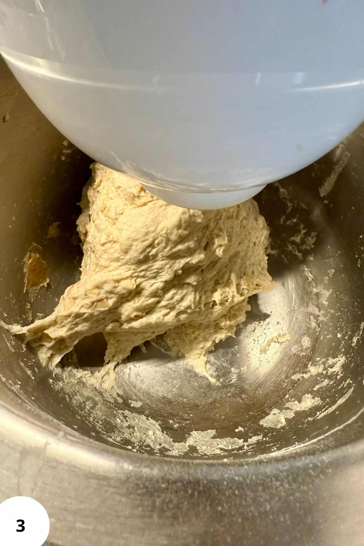 Mixer blending dough mixture in a mixing bowl.