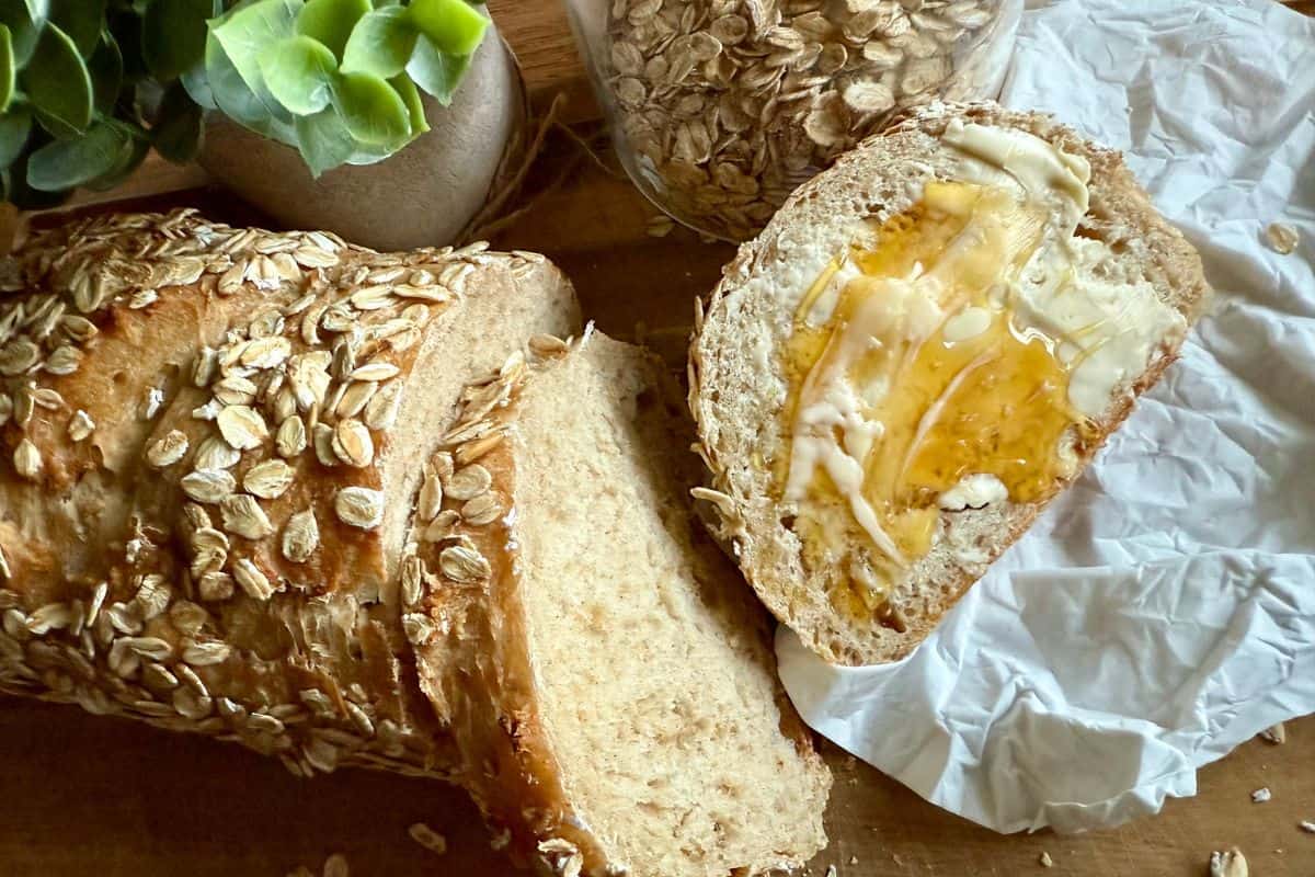 Freshly baked loaf of bread with a buttered slice beside it on a wooden board.