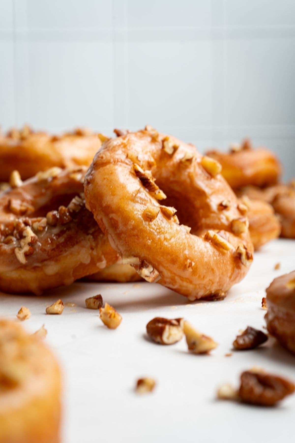 Maple glazed donuts on a surface scattered with chopped nuts.