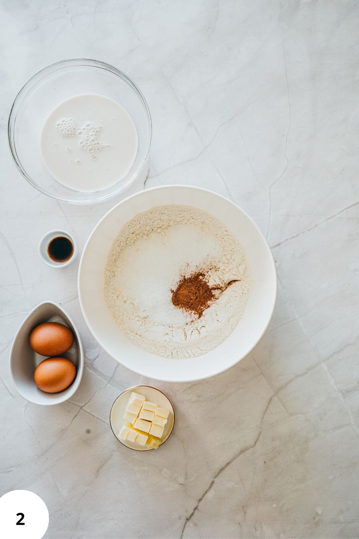 Donut ingredients being mixed in a large bowl surrounded by other baking ingredients.