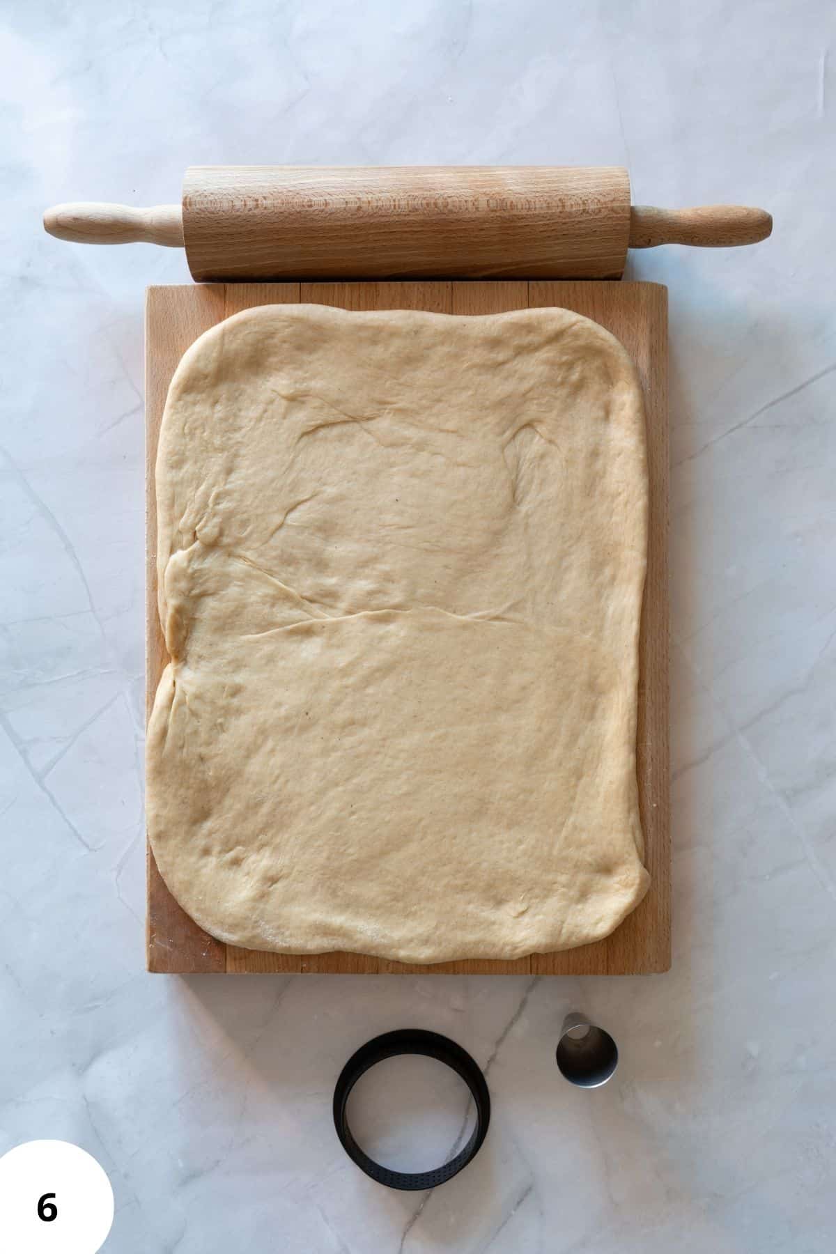 Flattened maple donut dough resting on a floured wooden board, ready to be cut into rings.