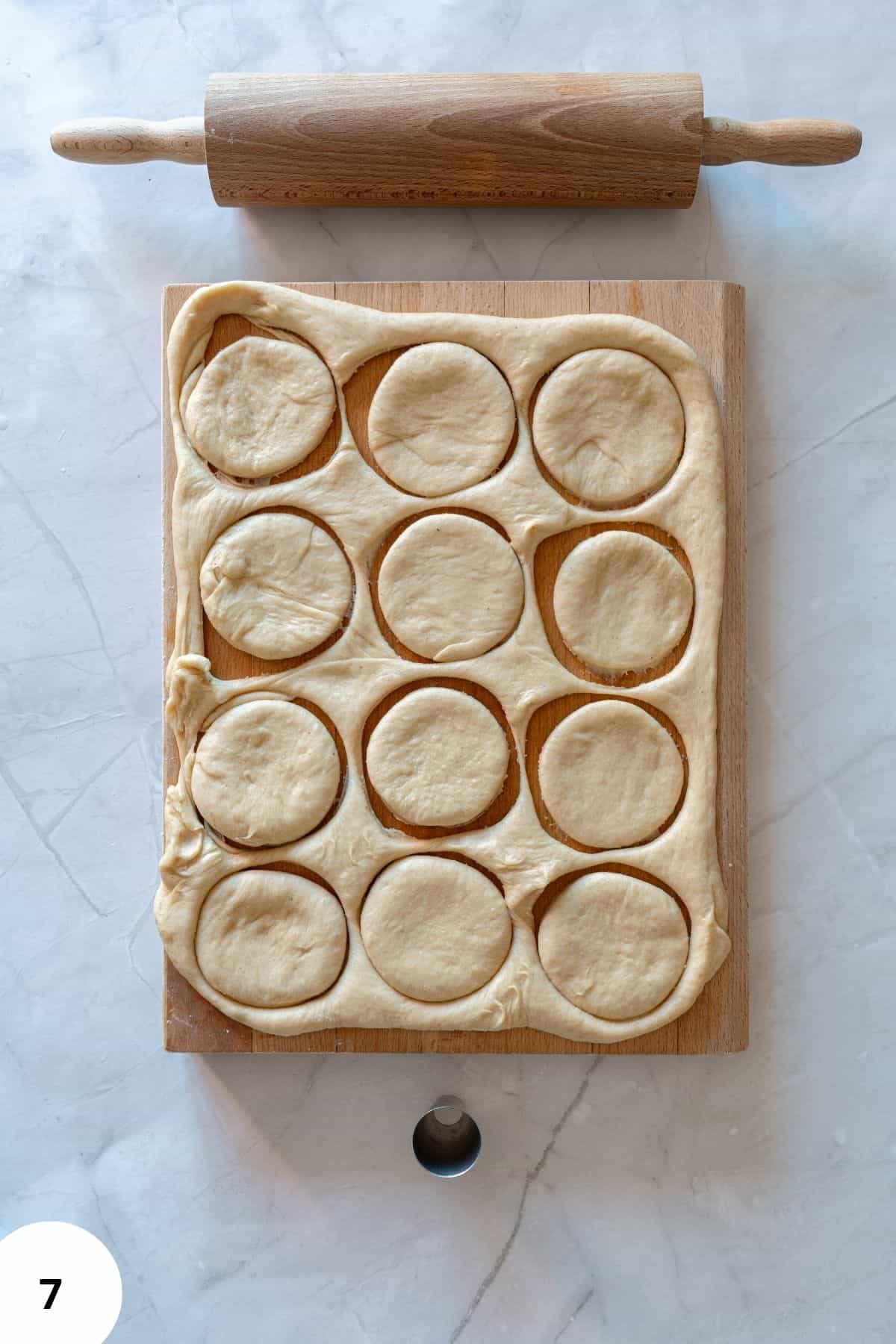 Donut dough being shaped into circles on a wooden board.