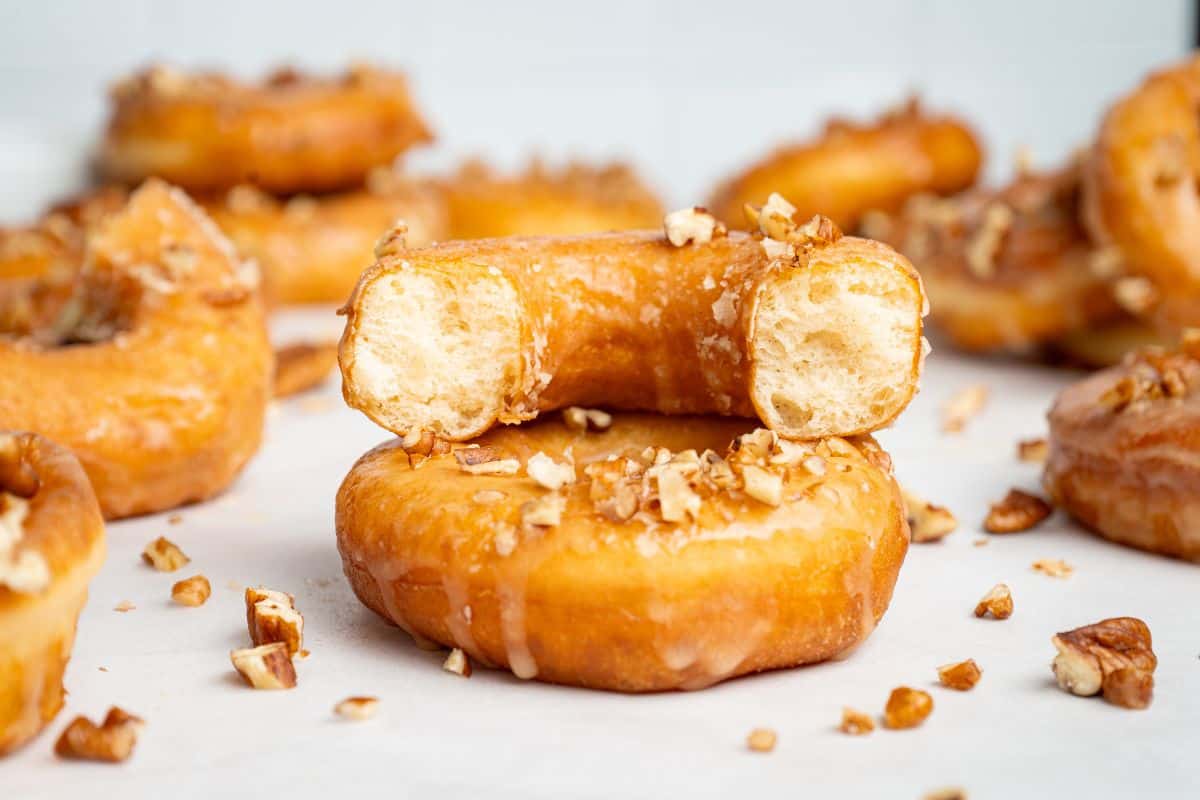 Maple glazed donuts on a surface scattered with chopped nuts.
