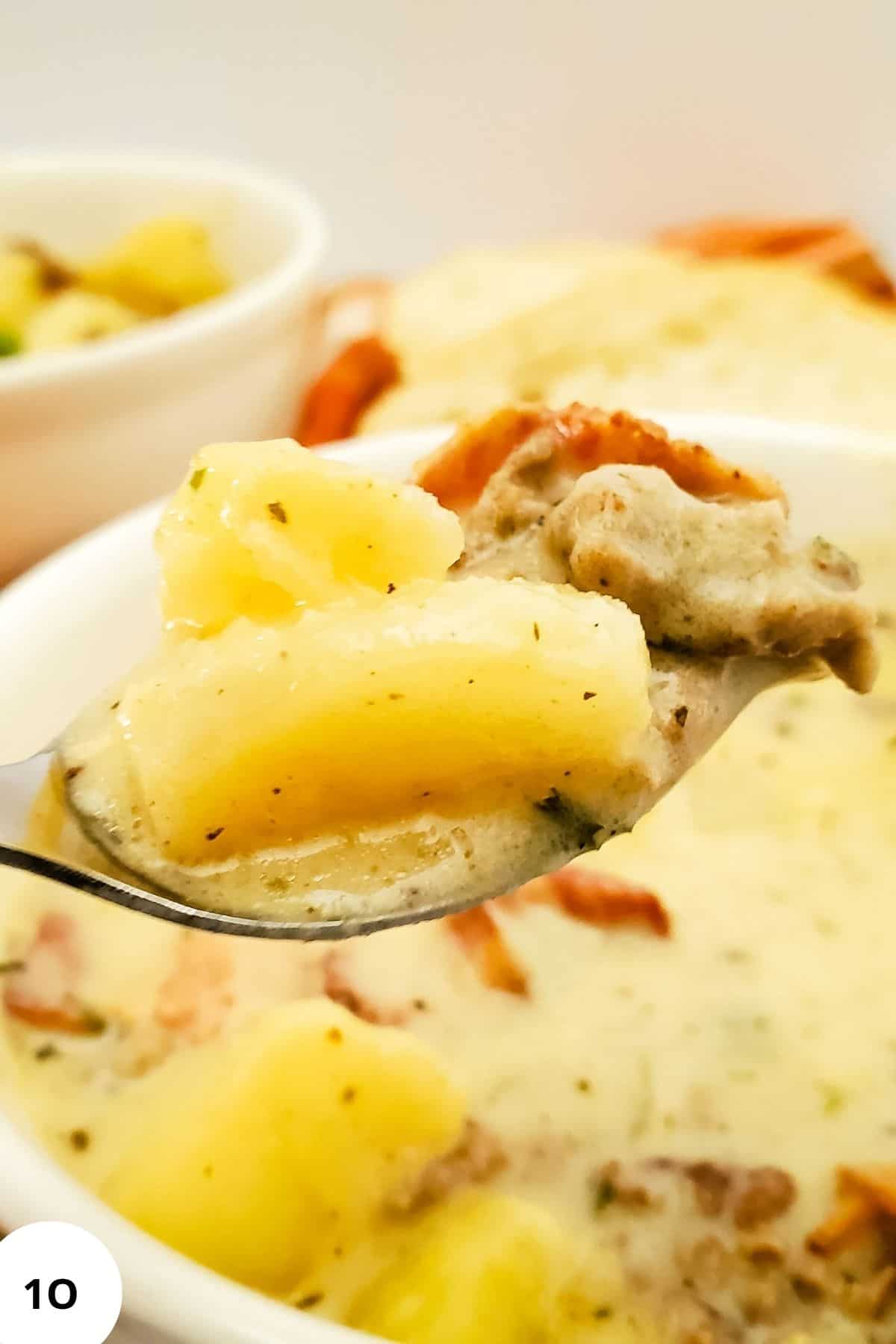 Close-up of creamy cheeseburger potato soup being lifted by a spoon, showing melted cheese and chunks of potatoes and bacon.