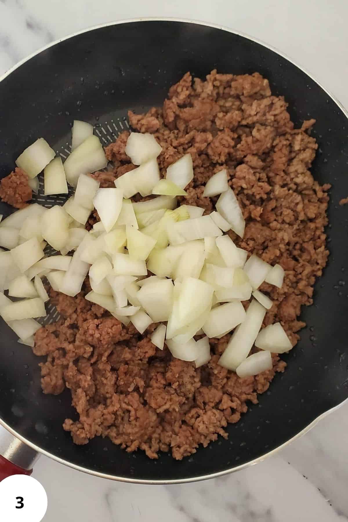 Ground beef in a skillet with seasonings and diced onions.
