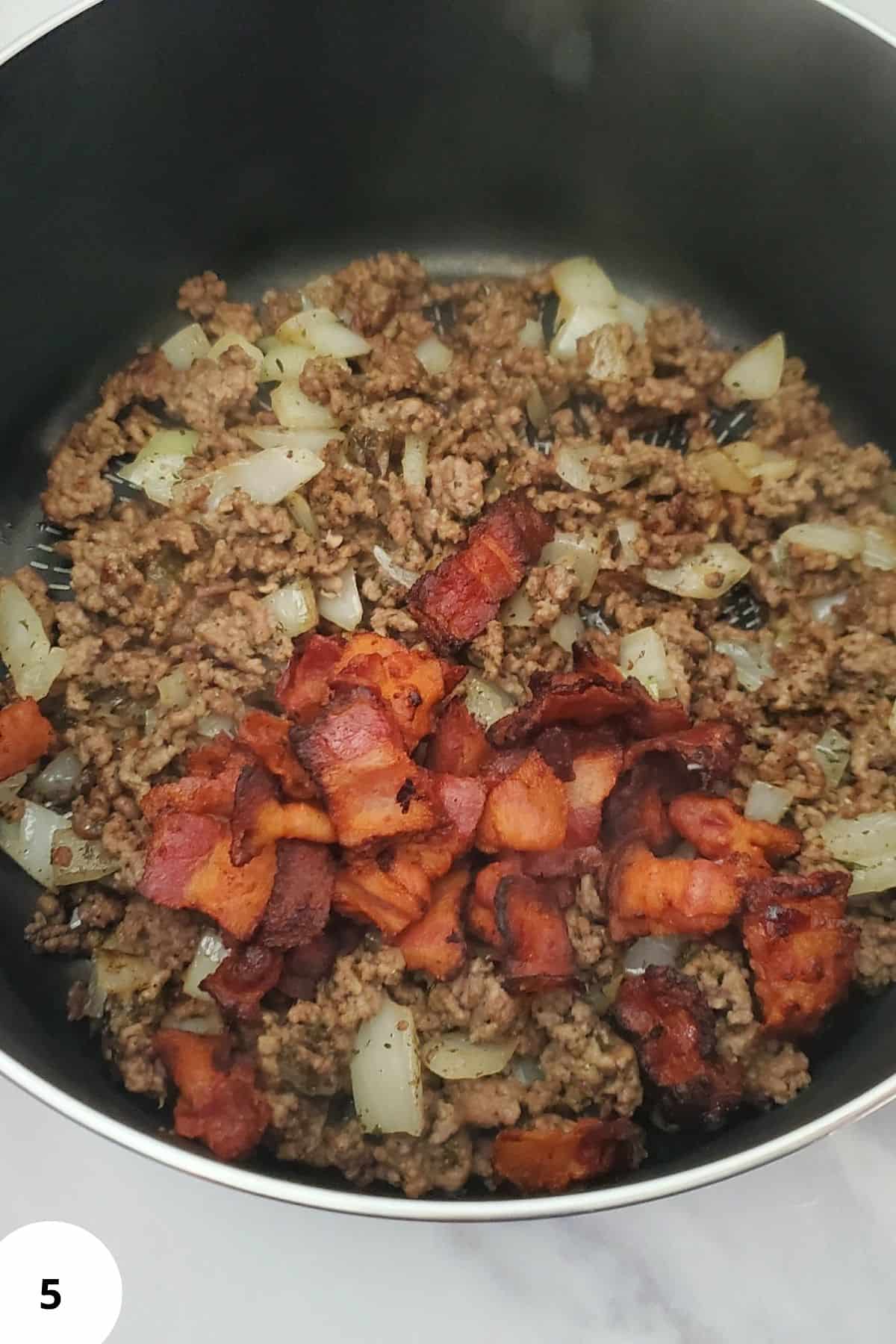 Ingredients in a pot with bacon visible, preparing to cook a creamy cheeseburger potato soup.