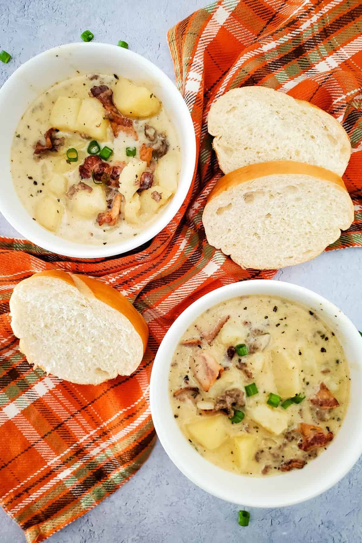 Creamy cheeseburger potato soup served in two bowls on a table with a napkin underneath, accompanied by garlic bread on the side.