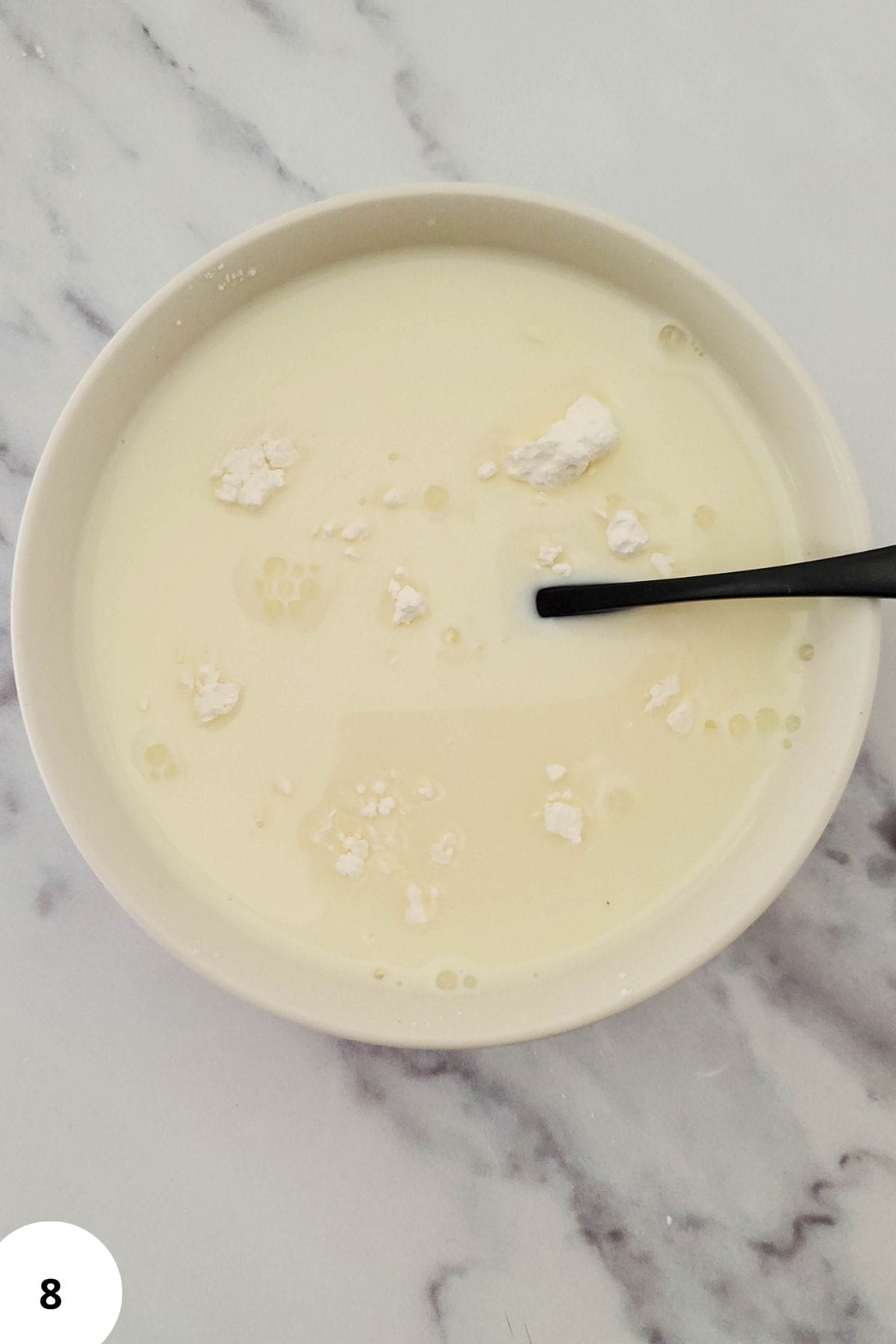 Cornstarch and milk mixture in a bowl with a spoon resting inside.