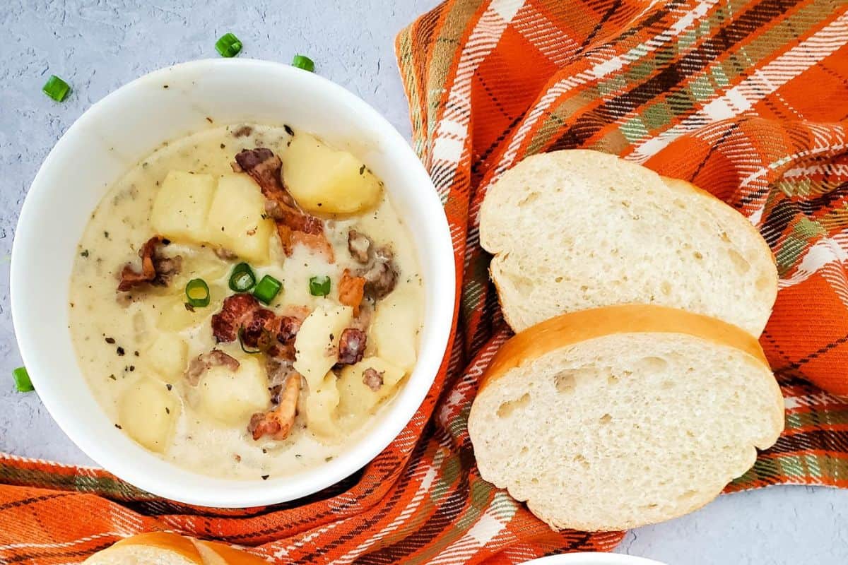 Creamy cheeseburger potato soup served in bowl on a table with a napkin underneath, accompanied by garlic bread on the side.