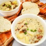 Creamy cheeseburger potato soup served in two bowls on a table with a napkin underneath, accompanied by garlic bread on the side.