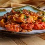 Close-up of oven-baked cheesy tortellini served on a plate, garnished with fresh herbs.