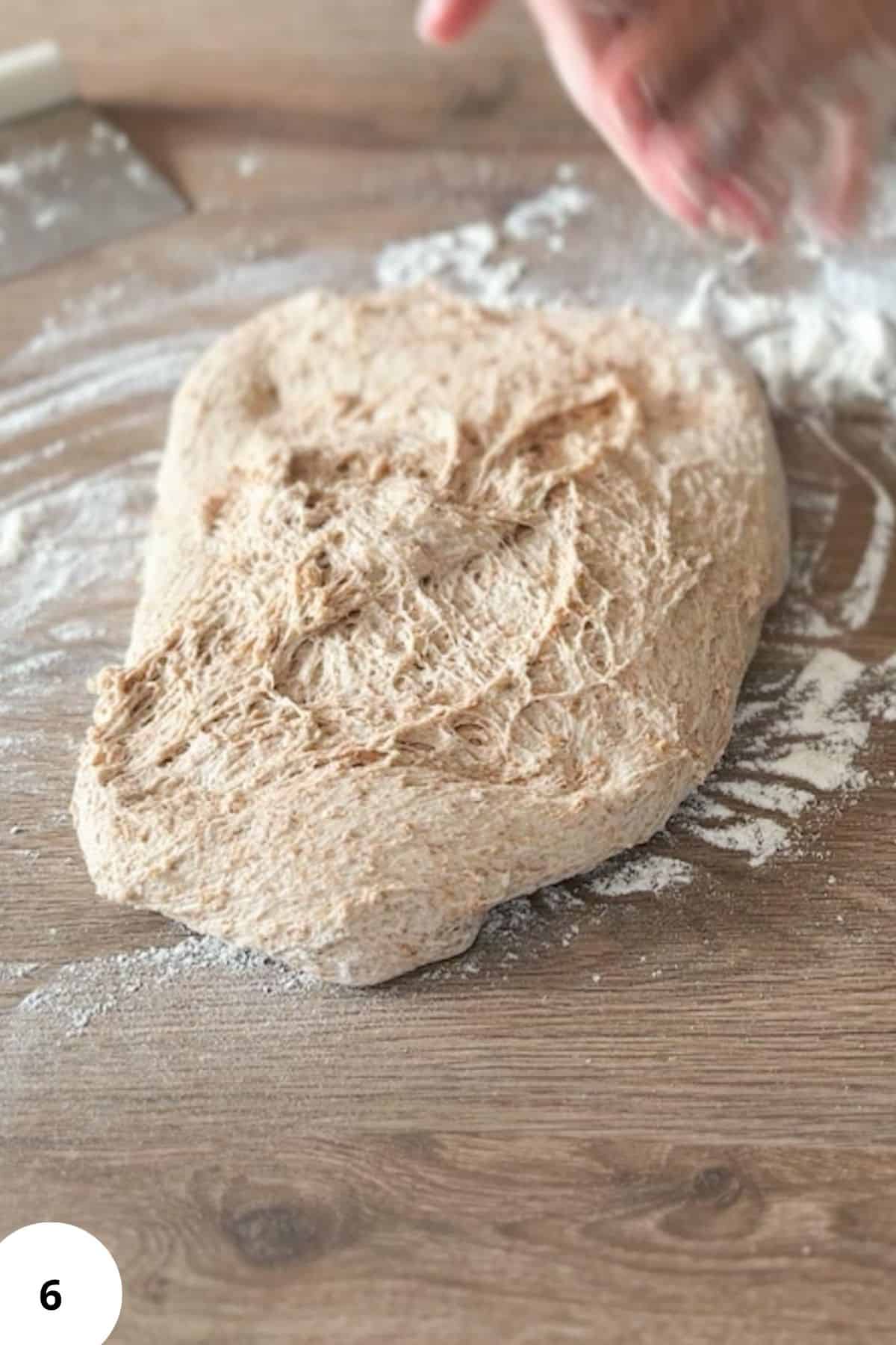 Lightly dusted dough sitting on a floured wooden surface.
