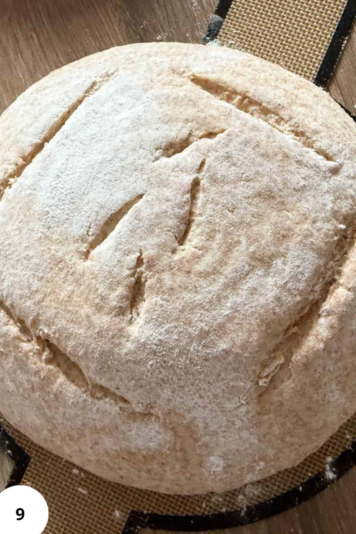 A lightly floured sourdough loaf placed on a rustic wooden board.