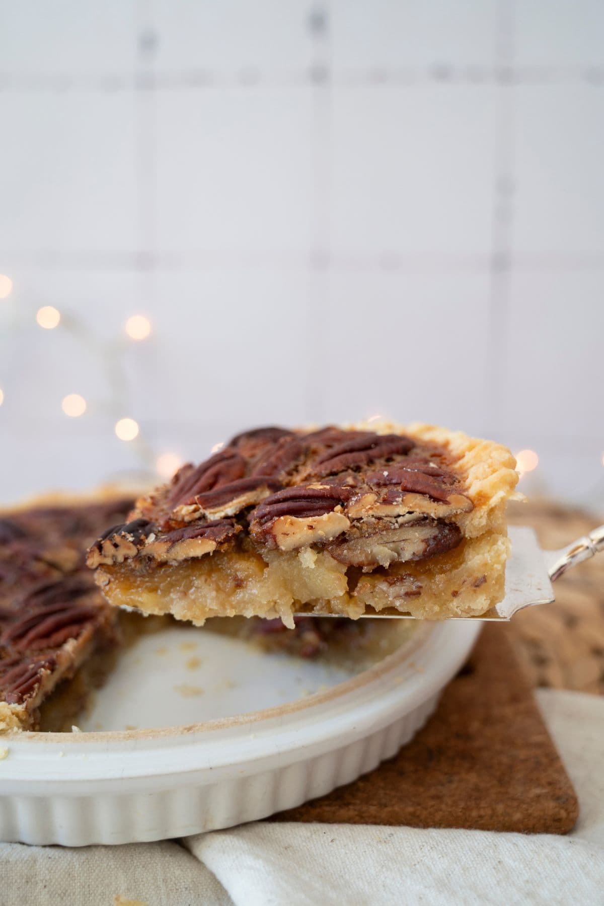A hand lifting a slice of pecan pie from the whole pie.