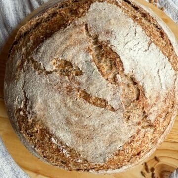 Freshly baked sourdough loaf resting on a rustic wooden board.