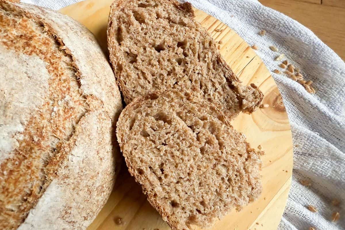 Sliced sourdough bread with the remaining loaf beside it on a wooden board.