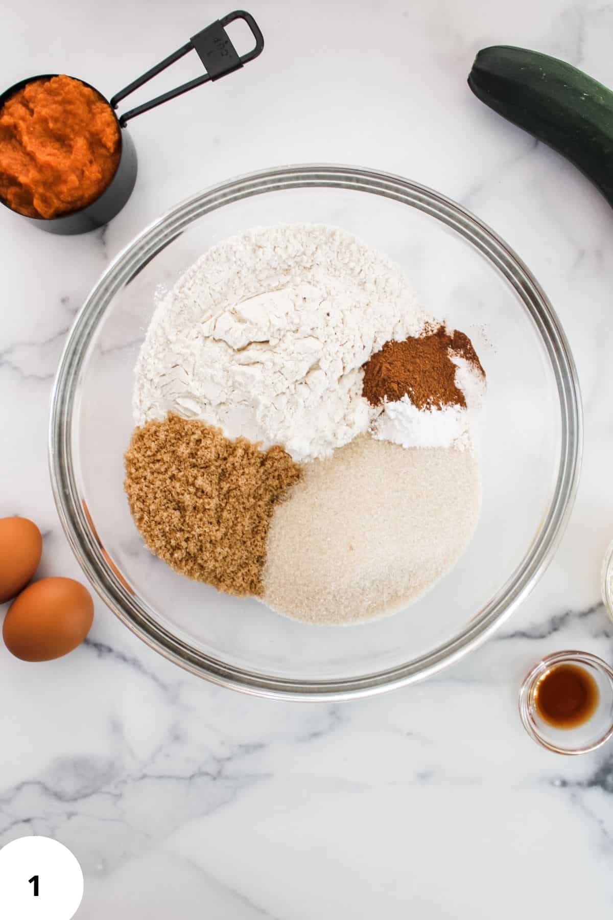A large bowl with dry ingredients including flour, baking soda, baking powder, salt, cinnamon, and pumpkin pie spice being mixed together.