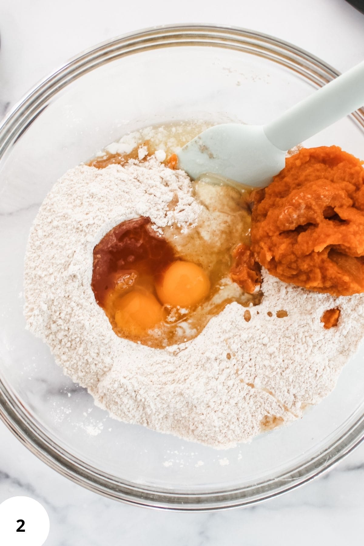Wet and dry ingredients being mixed together in a large bowl with a spatula resting on the edge.
