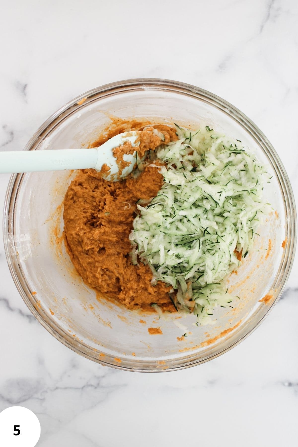 Wet and dry ingredients combined in a large bowl with shredded zucchini being gently mixed into the batter.