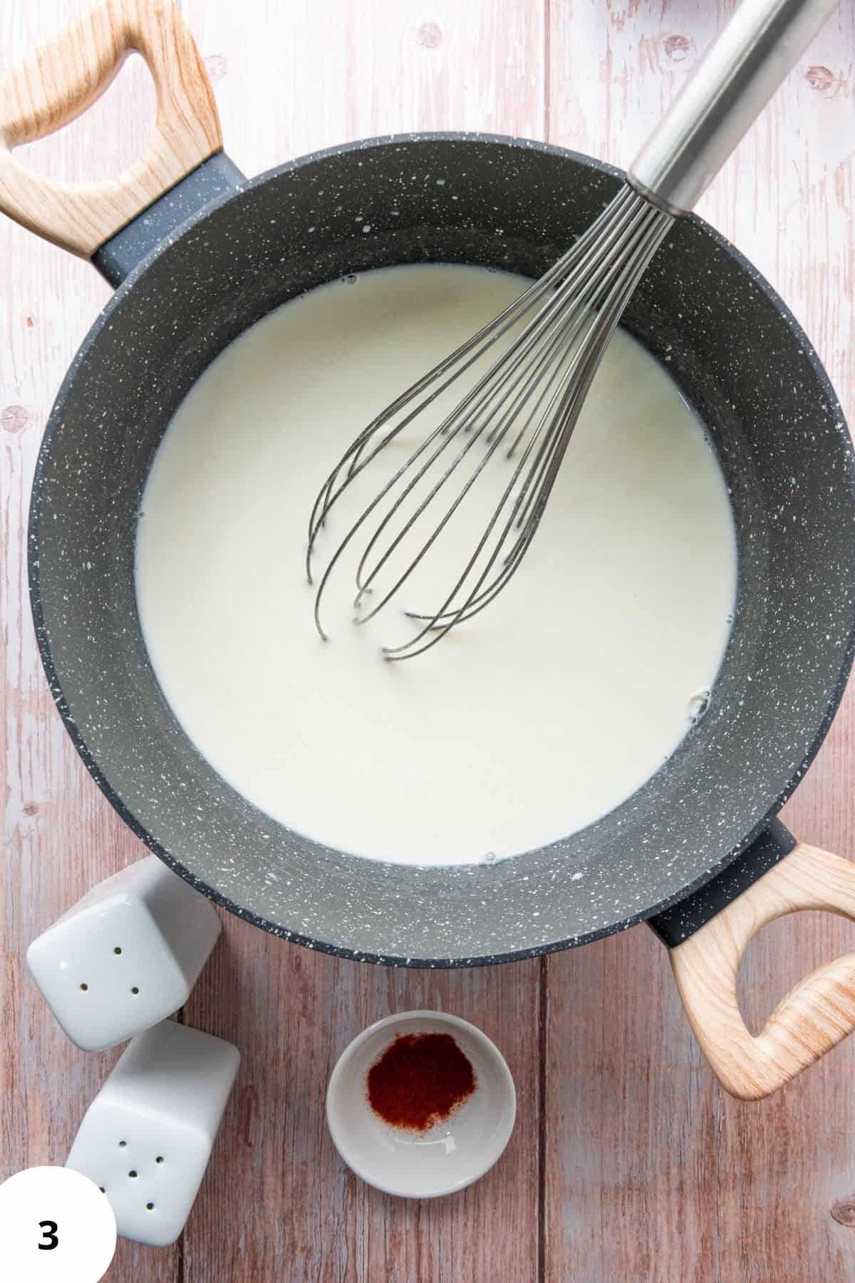 Mixture in a saucepan with a whisk resting on the edge.