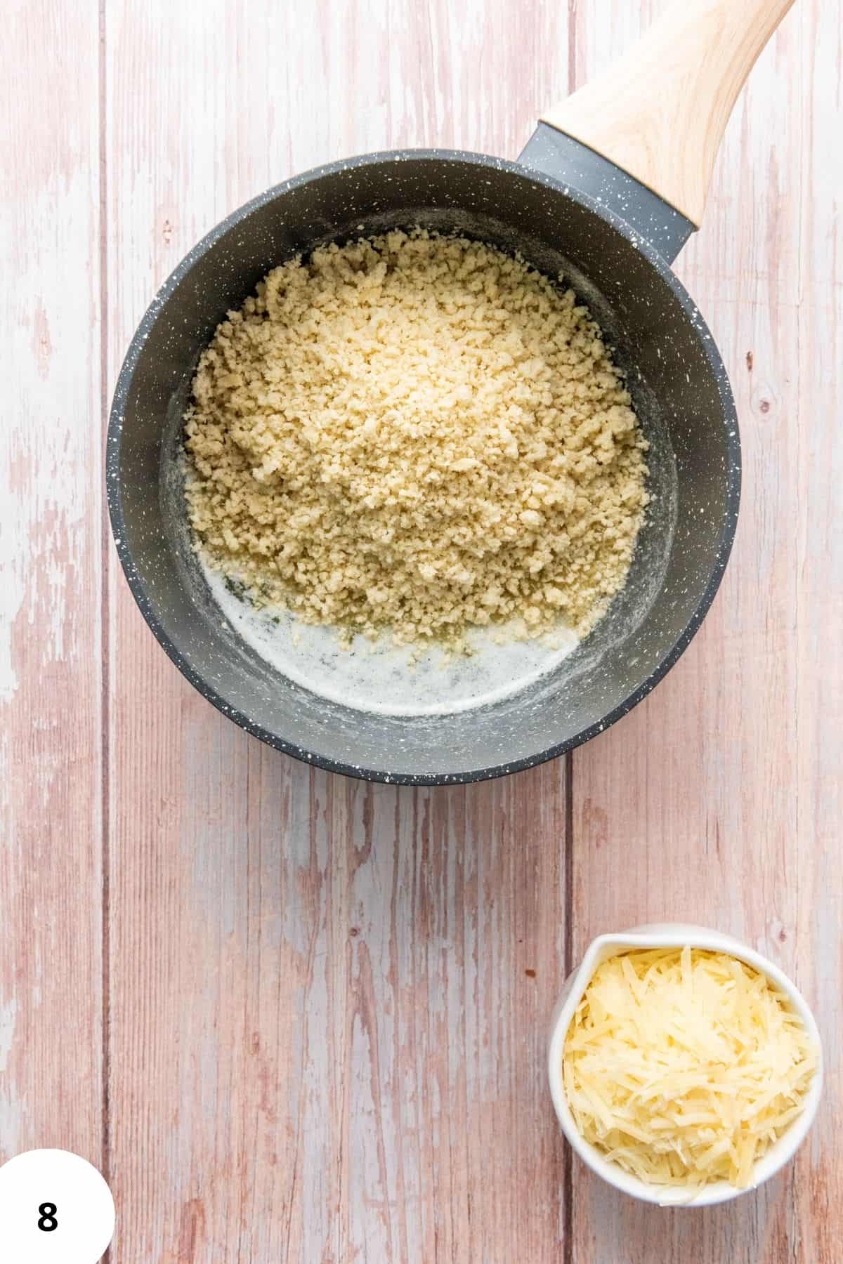 Butter and panko in a small saucepan with a pile of shredded cheese beside it.
