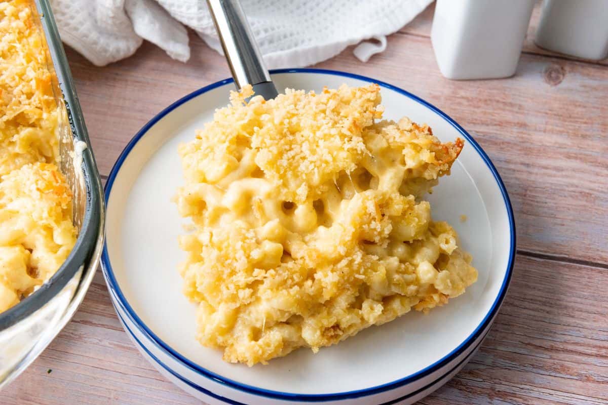 Macaroni served on a plate with the baking dish in the background holding the remaining macaroni.