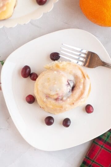 A single cranberry orange sourdough brioche roll on a plate with a fork, surrounded by festive Christmas ornaments.
