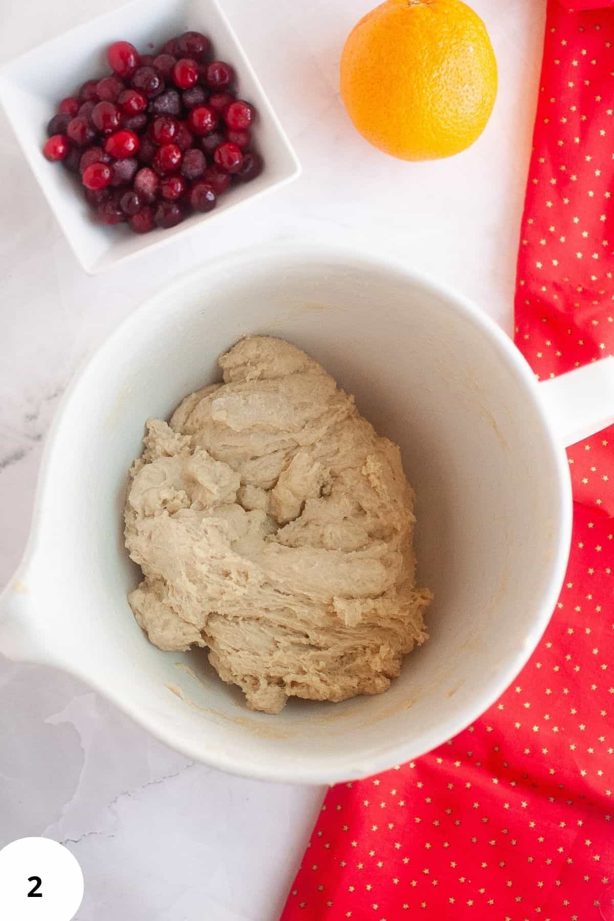Dough in a mixing bowl with cranberries on the side.