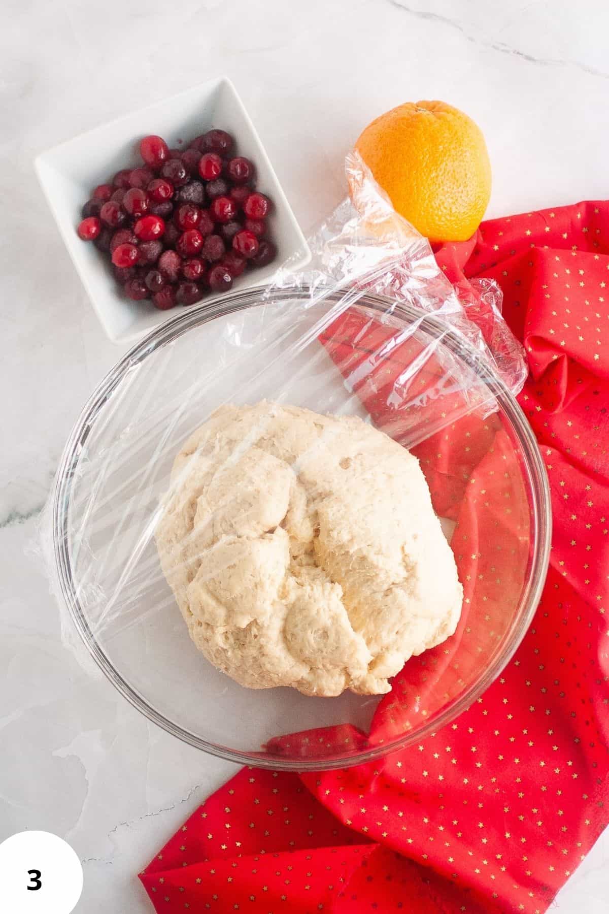 Dough in a large bowl, half covered with plastic.