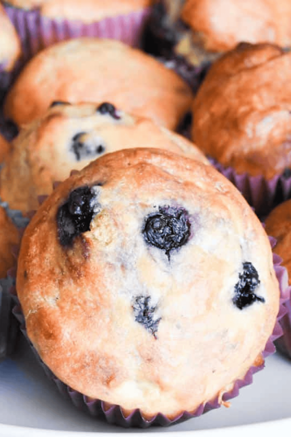 A close-up of fluffy sourdough blueberry muffins, showing golden-brown tops, juicy blueberries, and a soft, tender crumb inside.