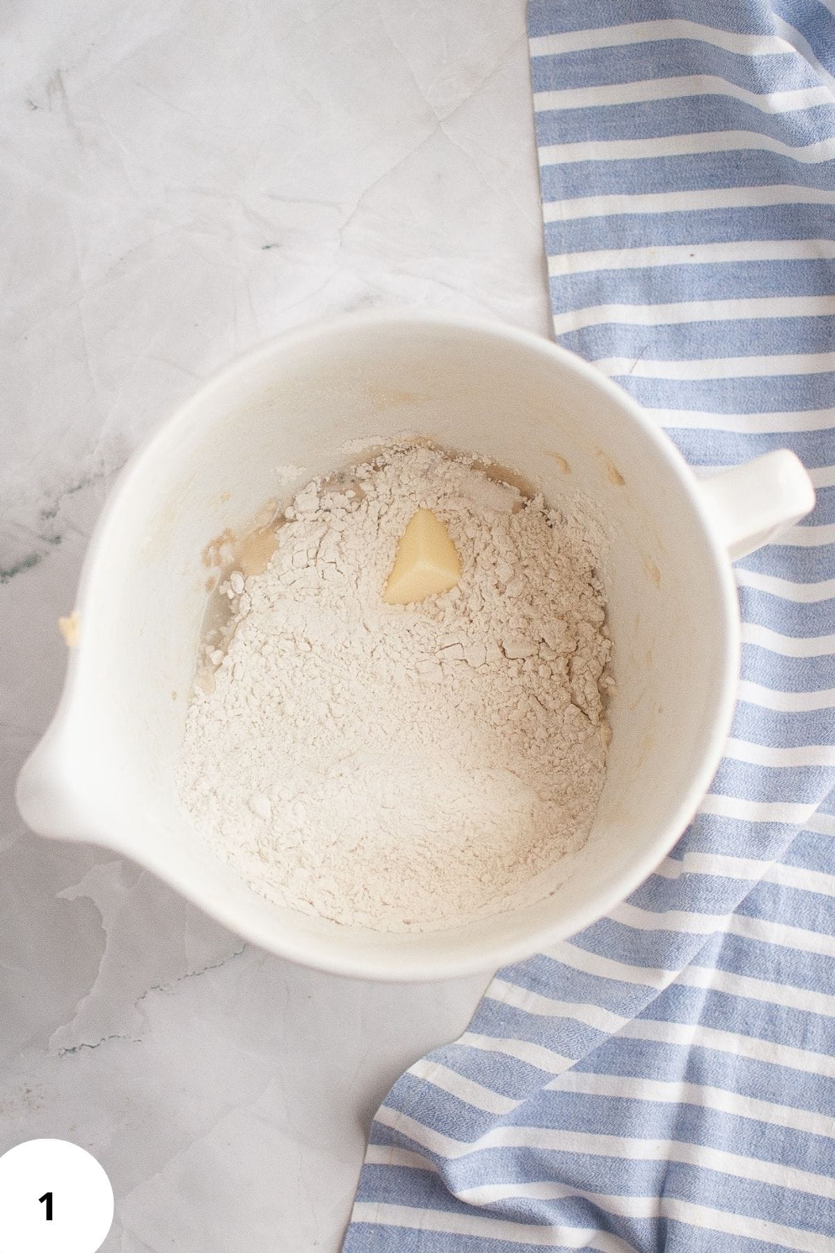 Ingredients for sourdough brioche rolls, flour, water, eggs, sugar, butter, salt, and sourdough starter-placed together in a mixing bowl, ready to be mixed.