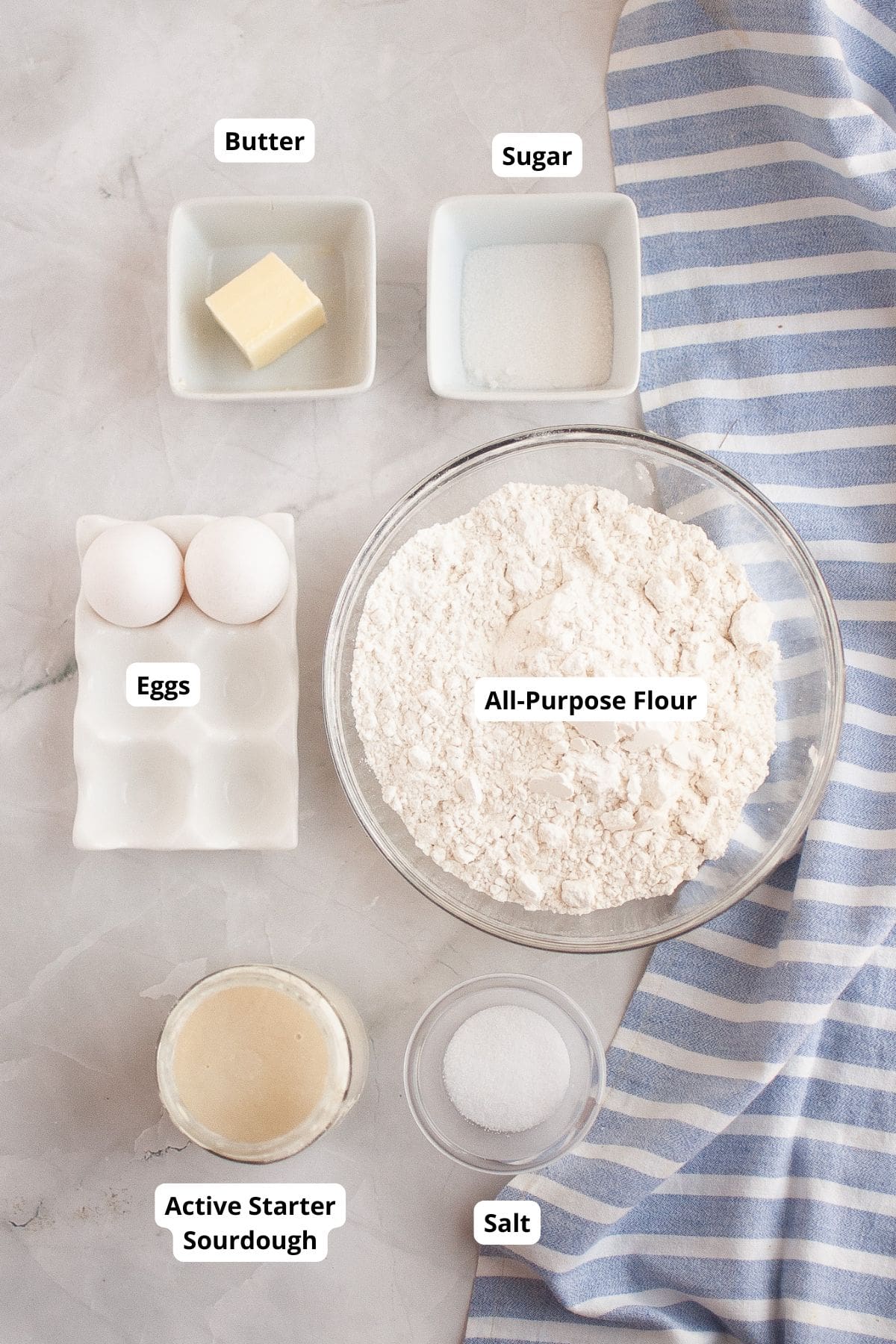 Ingredients for sourdough brioche rolls arranged on a marble surface with a table napkin on the side, ready for preparation.