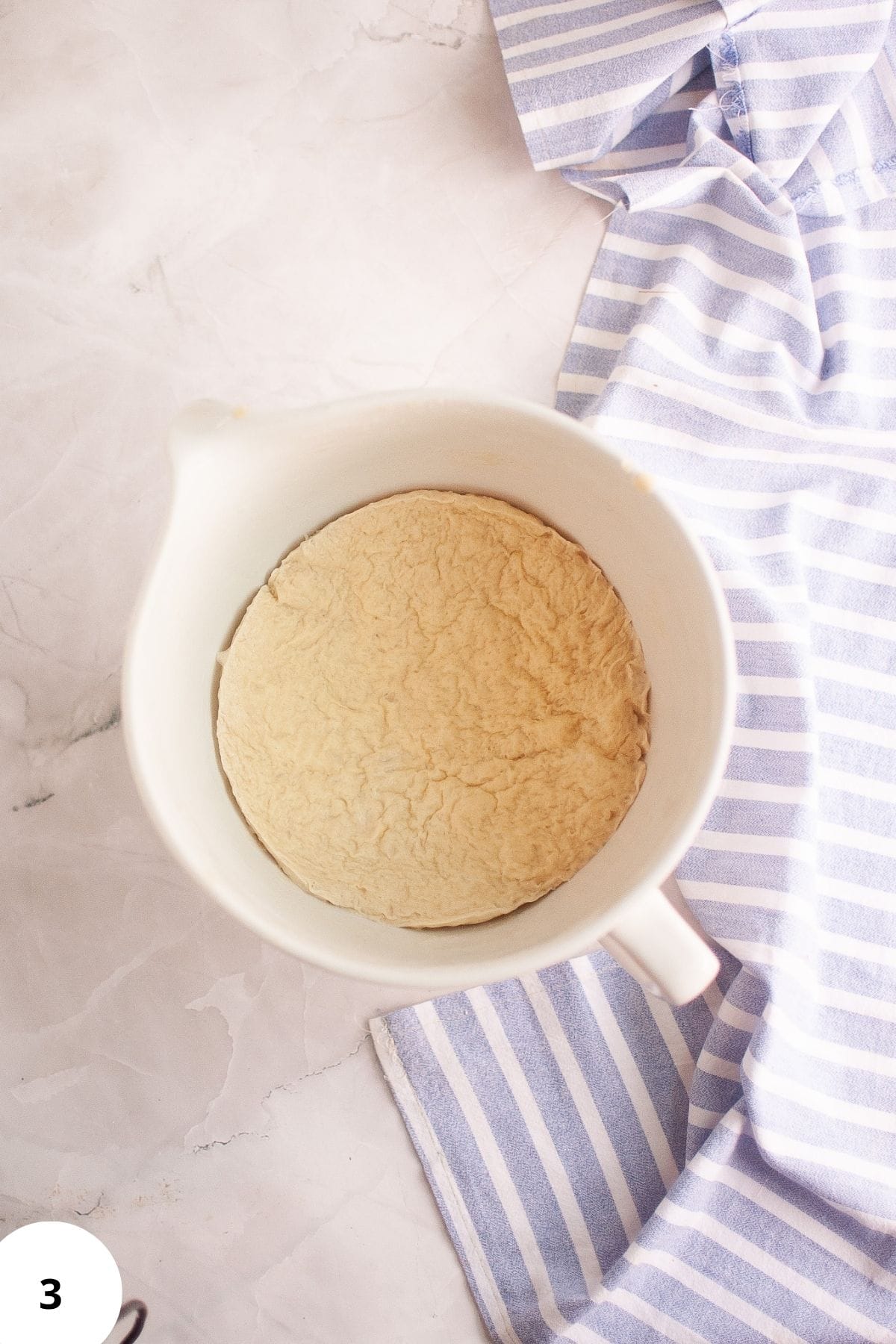 Sourdough brioche dough resting in a mixing bowl for fermentation, with a table napkin on the side.