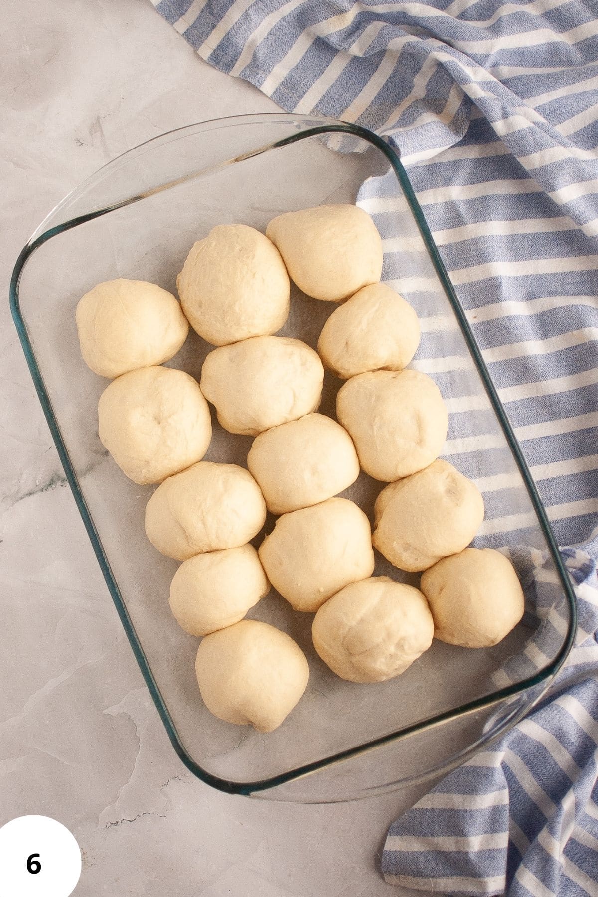Puffy sourdough brioche rolls in a baking dish, ready to bake, with a table napkin on the side.
