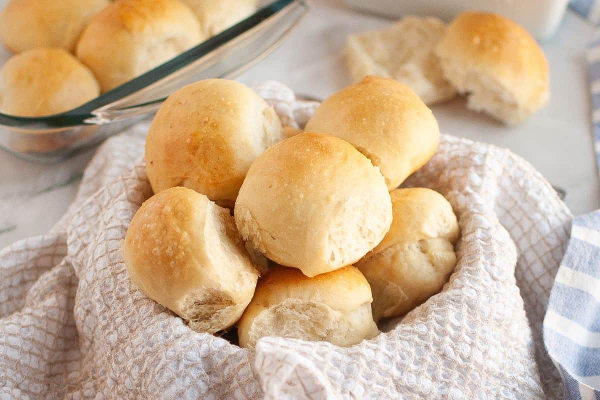 A basket lined with cloth filled with stacked sourdough brioche rolls.