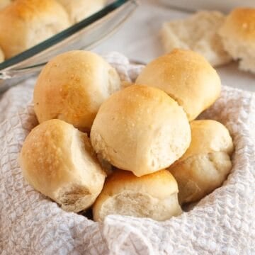 A basket lined with cloth filled with stacked sourdough brioche rolls.