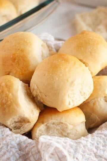 A basket lined with cloth filled with stacked sourdough brioche rolls.